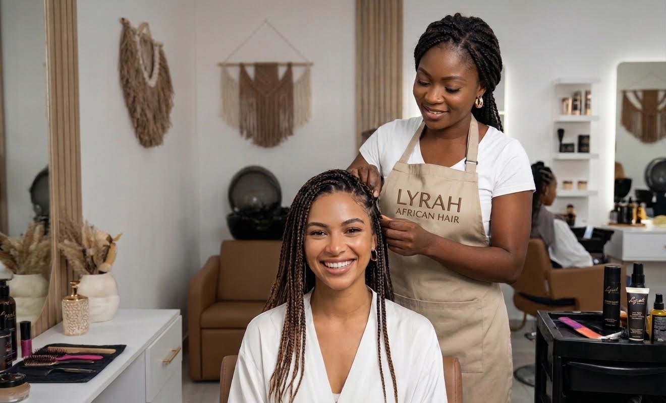 Smiling client with long box braids as a Lyrah braider finishes her style in the salon