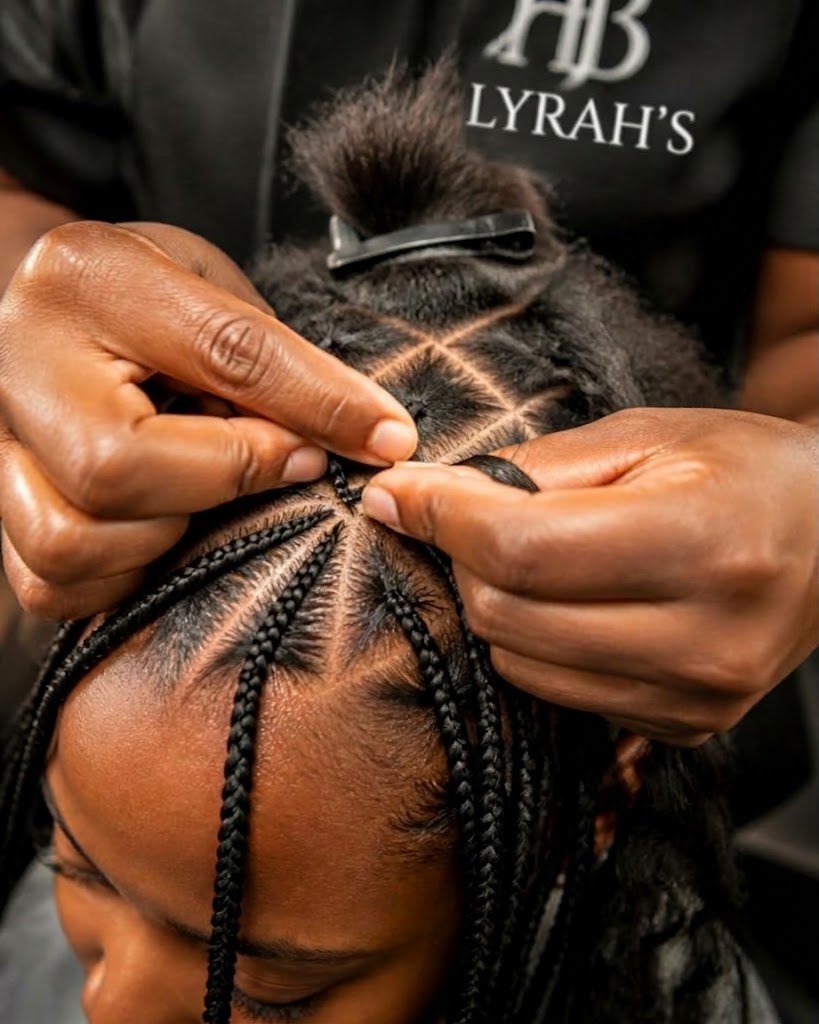 A Lyrah braider parting and braiding a client's hair into neat triangle-part box braids