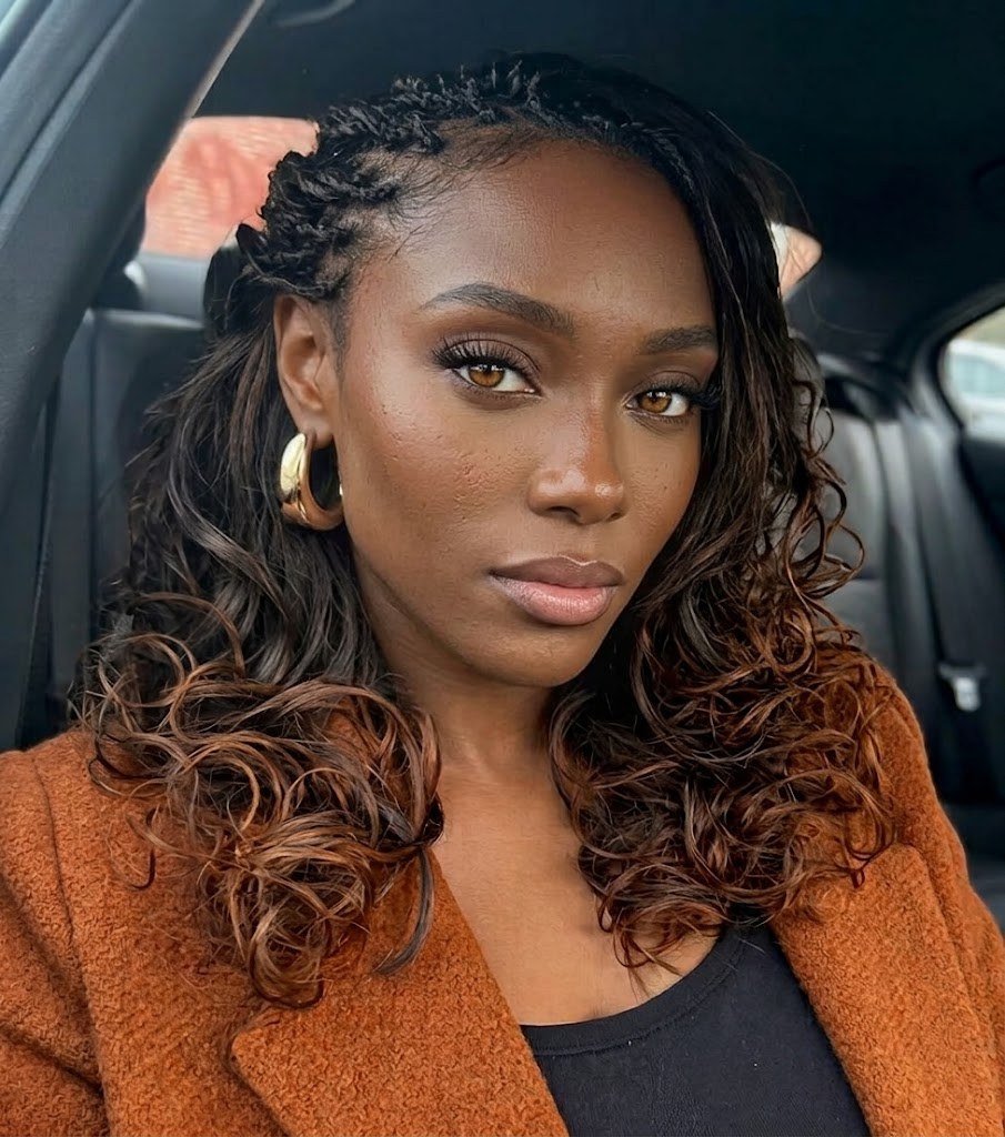 Woman with twisted cornrows on one side and long curly copper-brown hair, in a rust coat